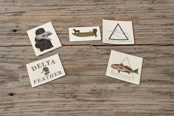 Set of six Delta Feather and Leg Lok duck stamp stickers on a wooden surface