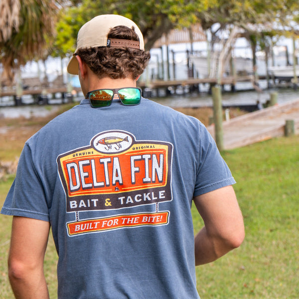 Person wearing a blue t-shirt with Delta Fin Bait & Tackle logo outdoors.