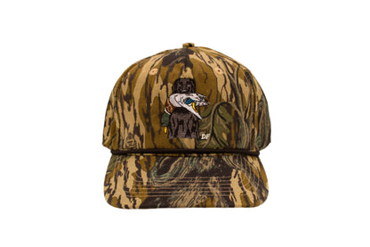 Camouflage baseball cap with a dog holding a mallard logo on a beige background