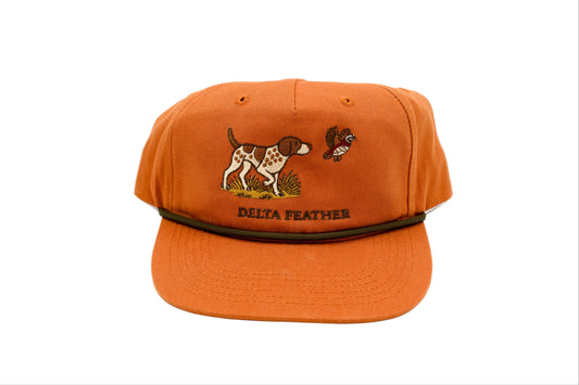 A burnt orange hat with a GSP pointing at a quail, with the words delta feather underneath 