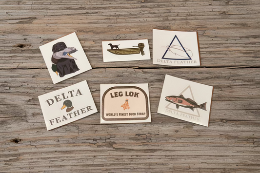Set of six Delta Feather and Leg Lok duck stamp stickers on a wooden surface
